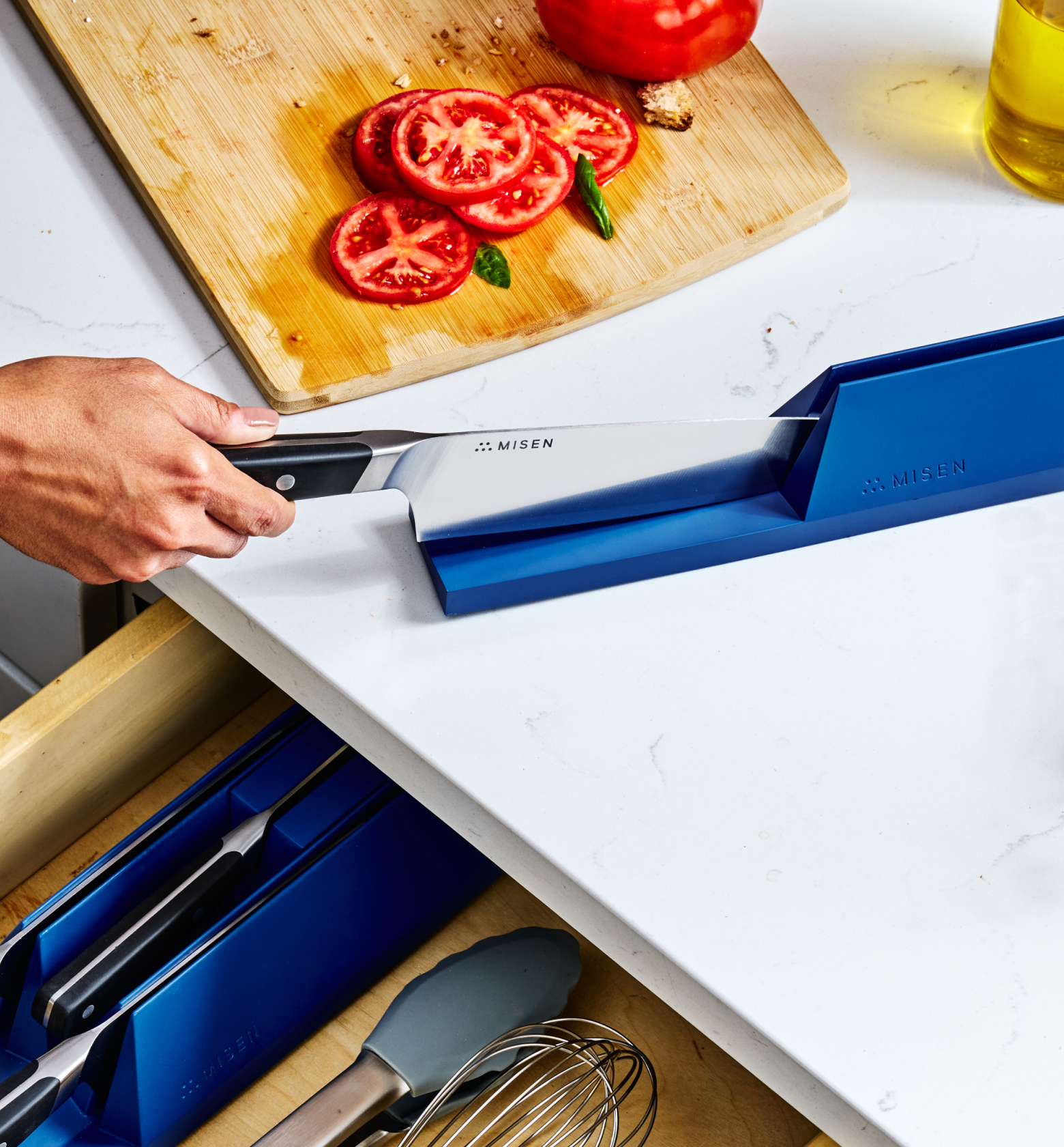 Misen chef's knife being sharpened with Misen blue knife sharpener on marble countertop