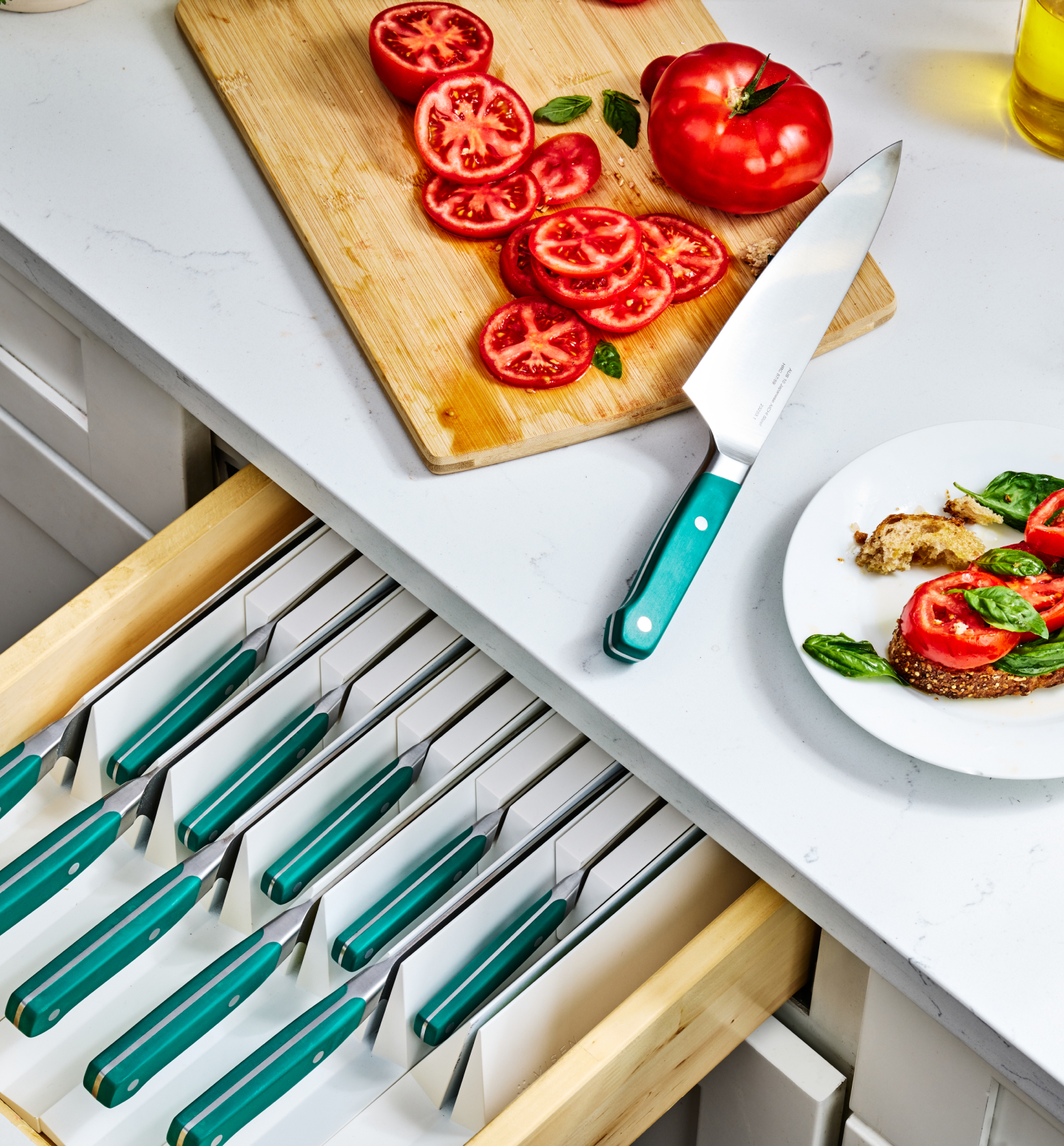 Teal-handled chef's knife set stored in drawer insert with sliced tomatoes on cutting board