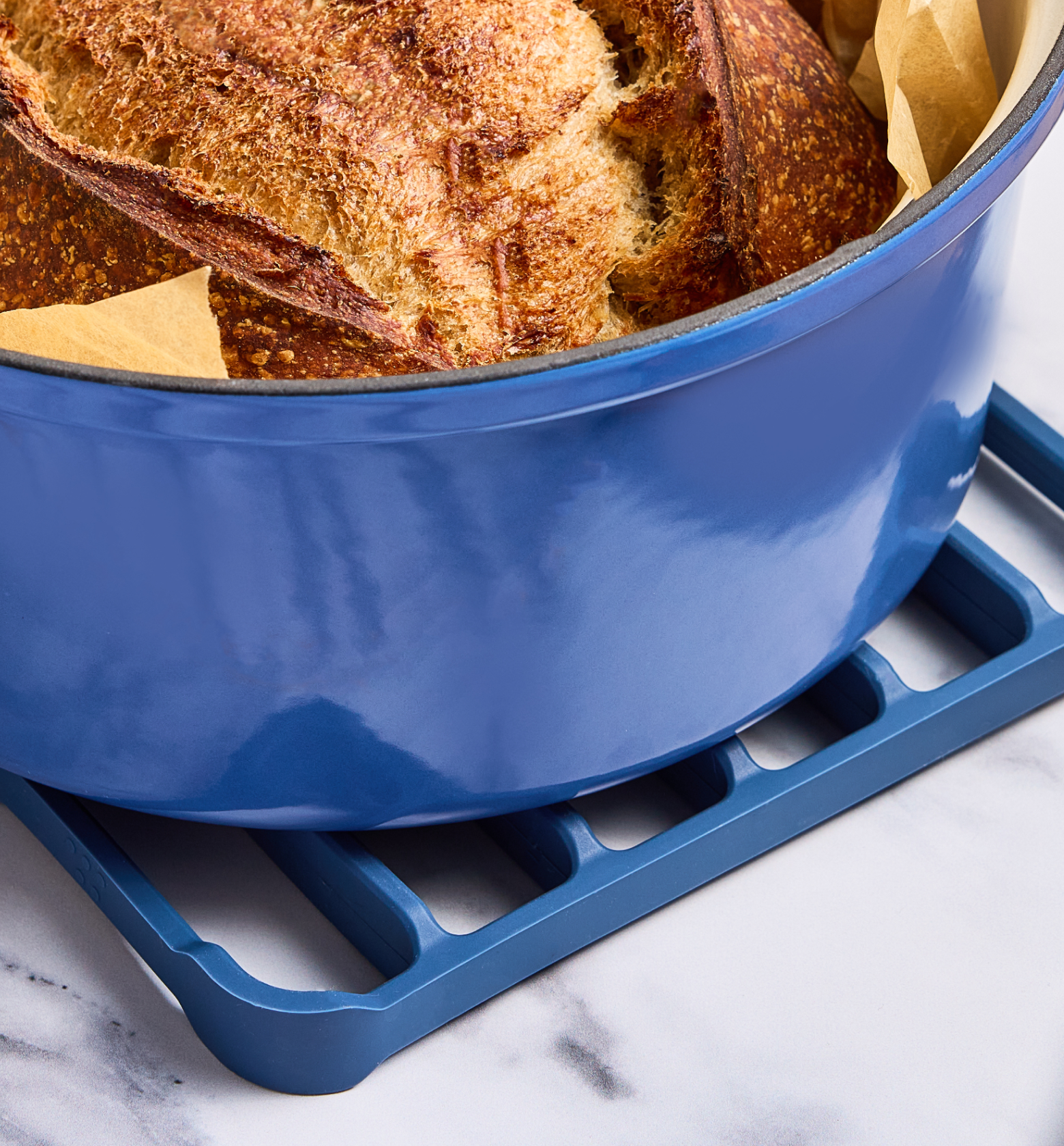 Freshly baked sourdough bread in a blue enameled cast iron Dutch oven on a matching trivet